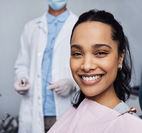 Woman with dark hair sitting in dental chair with pink bib about to undergo an examination