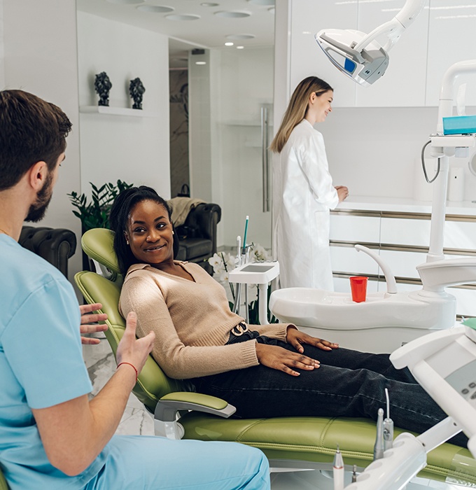 Woman in dental chair looking at dentist in blue scrubs speaking to her