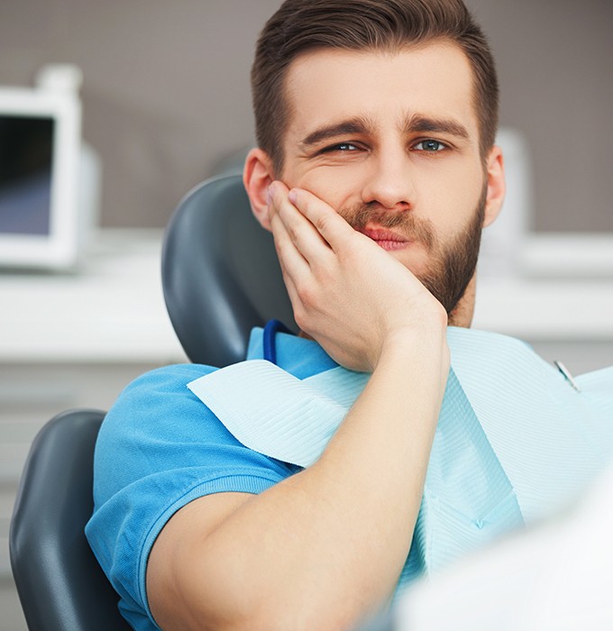 Male dental patient rubbing jaw in pain while visiting emergency dentist in Flint, MI