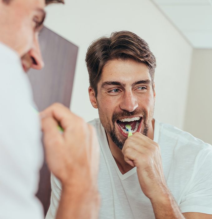 Man in white shirt brushing teeth in the mirror